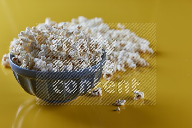 A blue pottery bowl full of popcorn with popcorn beside it on a yellow background in different angles