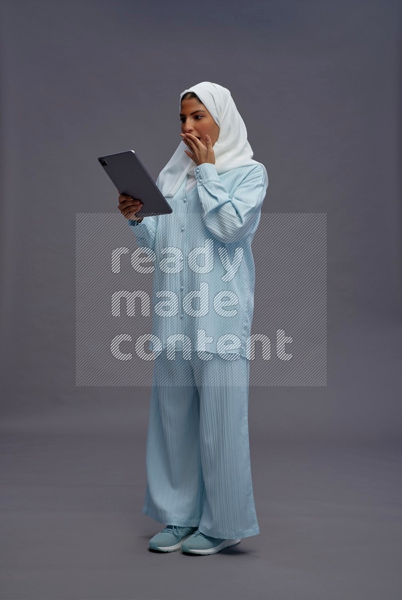 Saudi woman wearing hijab clothes standing working on tablet on gray background