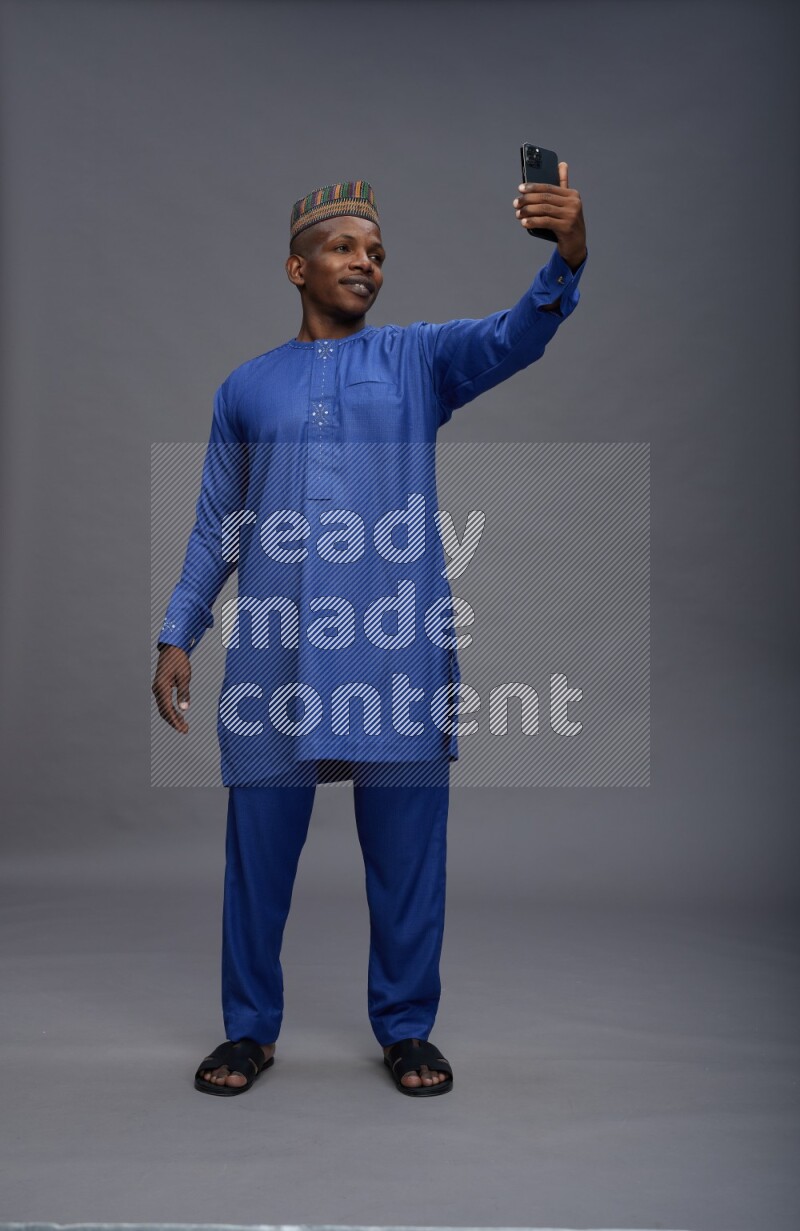 Man wearing Nigerian outfit standing taking selfie on gray background