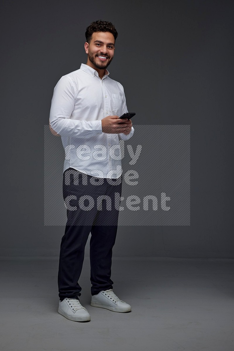 A man wearing smart casual standing and using his phone eye level on a gray background