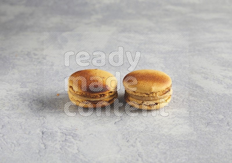 45º Shot of two Yellow Crème Brulée macarons on white  marble background