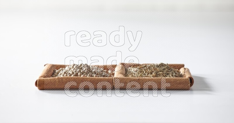 مربعان من أعواد القرفة ممتلئان بحبوب الفلفل الأبيض وحبوب الكمون علي خلفية بيضاء