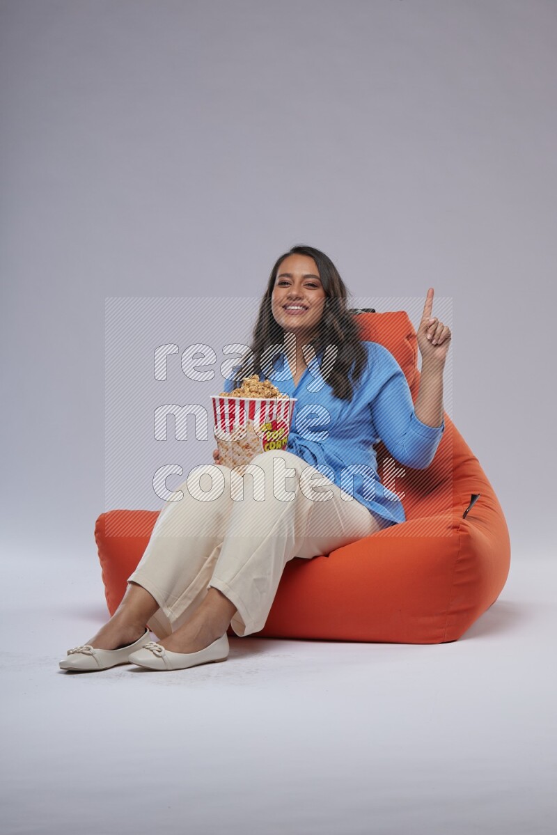 A woman sitting on an orange beanbag and eating popcorn