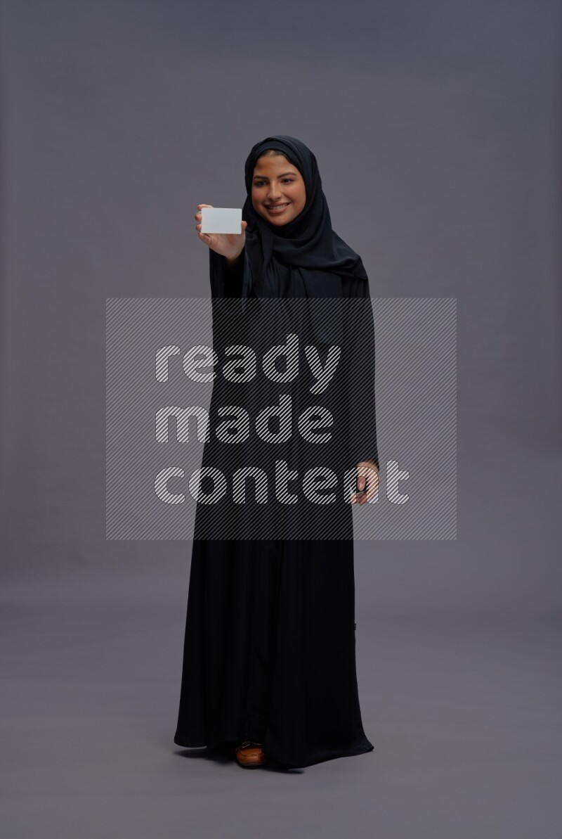 Saudi woman wearing Abaya standing holding ATM card on gray background