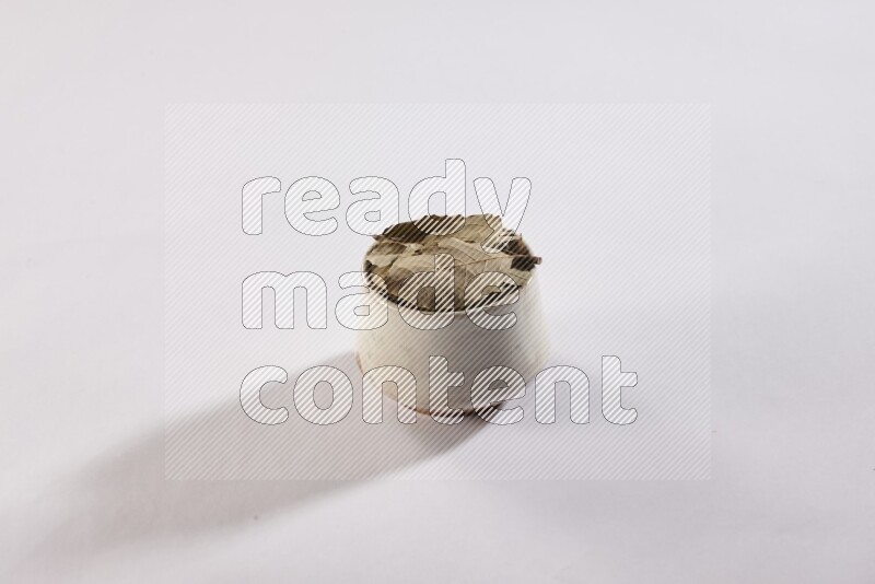 A beige pottery bowl full of dried bay leaves on white flooring