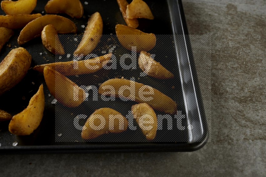 wedges potato in a black stainless steel rectangle tray on grey textured counter top