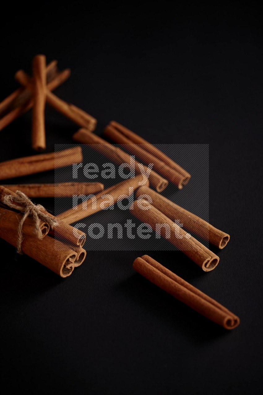 4 Cinnamon sticks stacked and bounded with more sticks in the background in different angles, black flooring