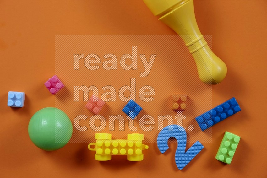 Plastic building blocks, balls and bowling pins on orange background in top view (kids toys)