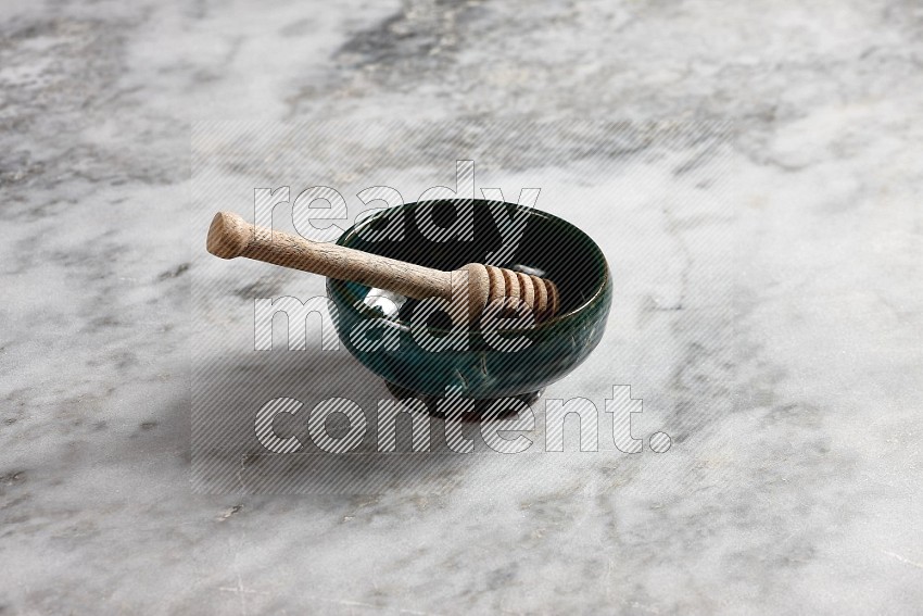 Dark green Pottery Plate with wooden honey handle in it, on grey marble flooring, 45 degree angle