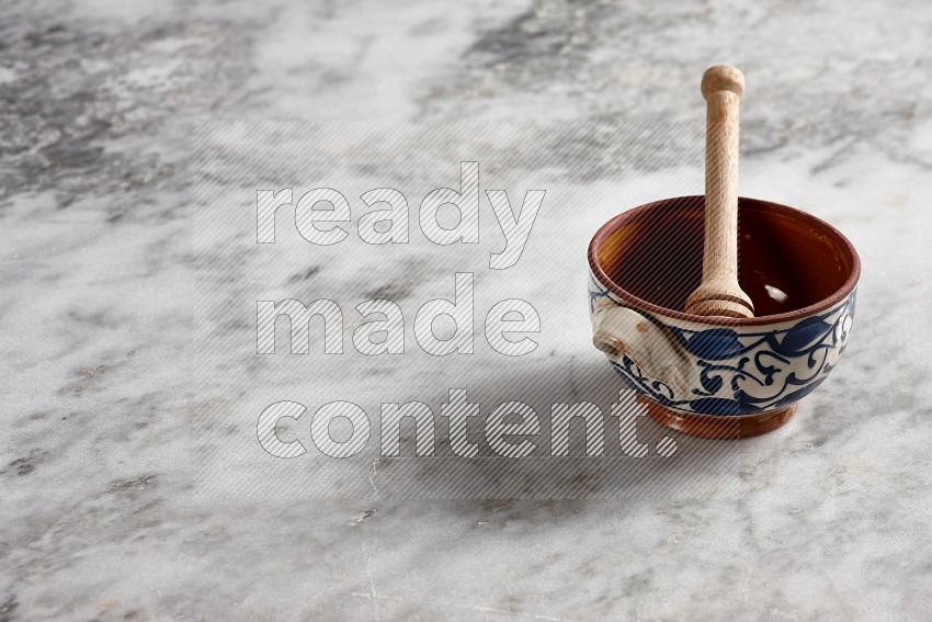 Decorative Pottery Pot with wooden honey handle in it, on grey marble flooring, 45 degree angle