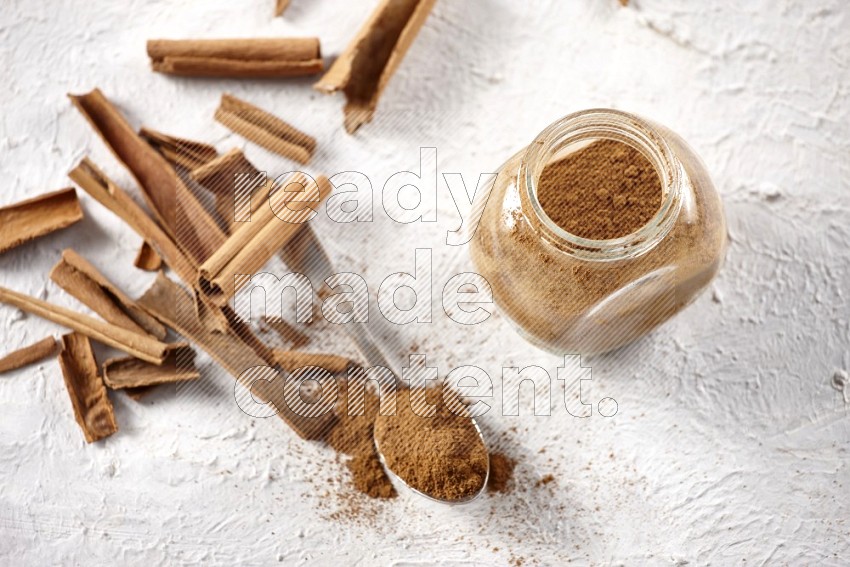 Herbal glass jar full cinnamon powder and a metal spoon full of powder surrounded by cinnamon sticks on a white background in different angles