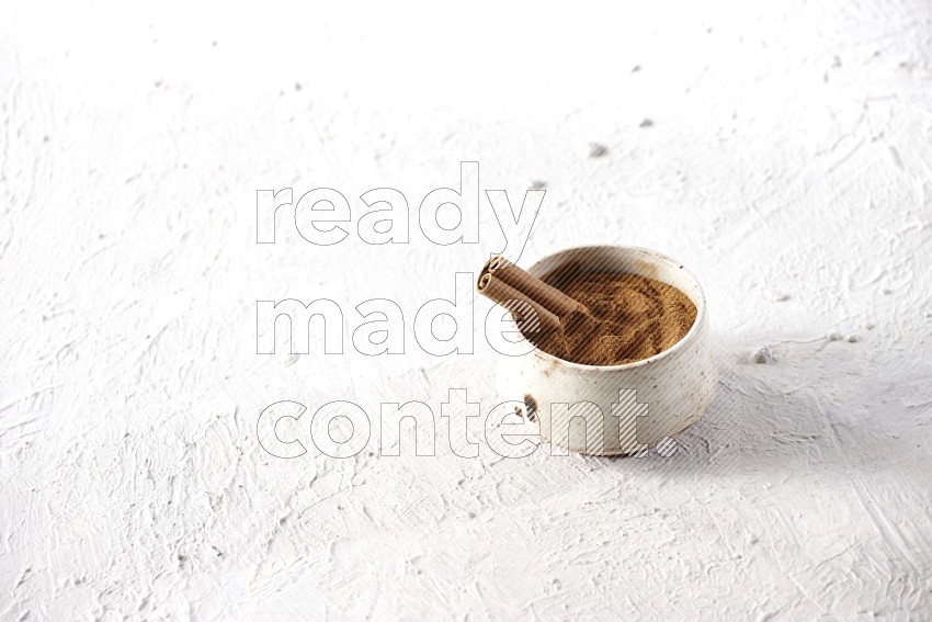 Ceramic beige bowl full of cinnamon powder with a cinnamon stick on a textured white background in different angles