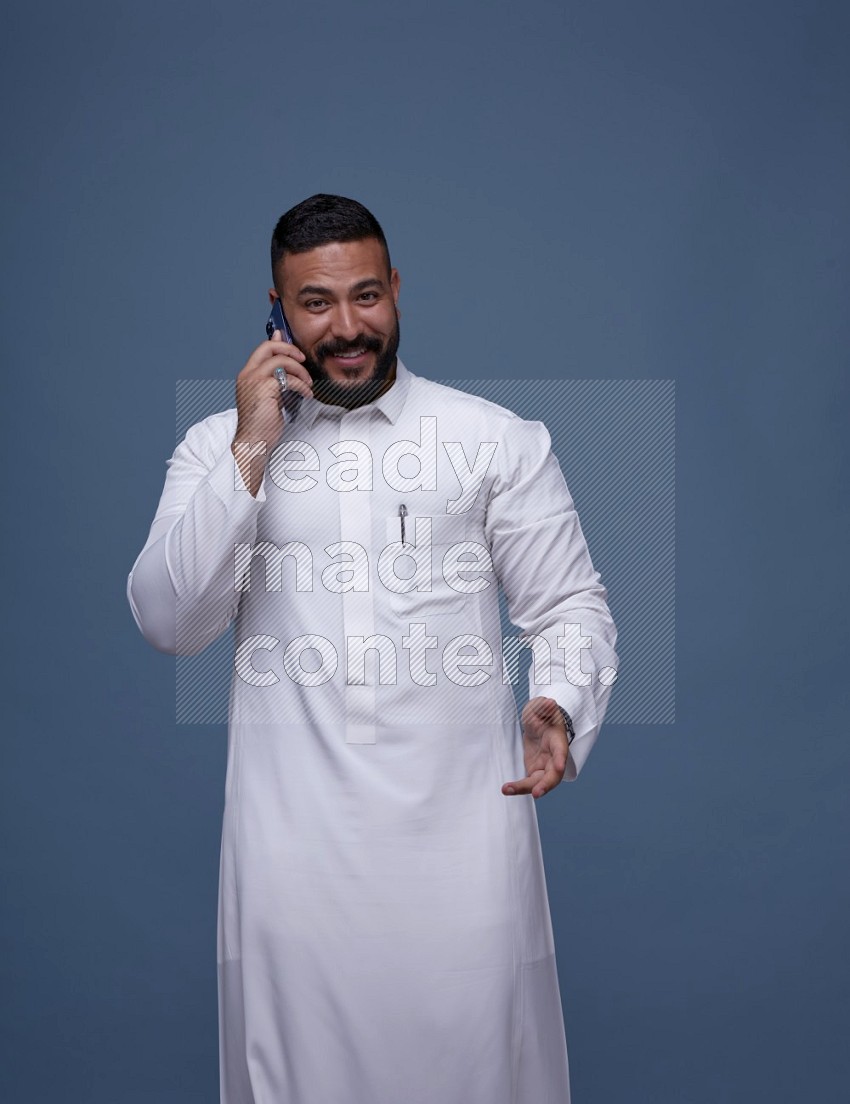A man Calling on Blue Background wearing Saudi Thob