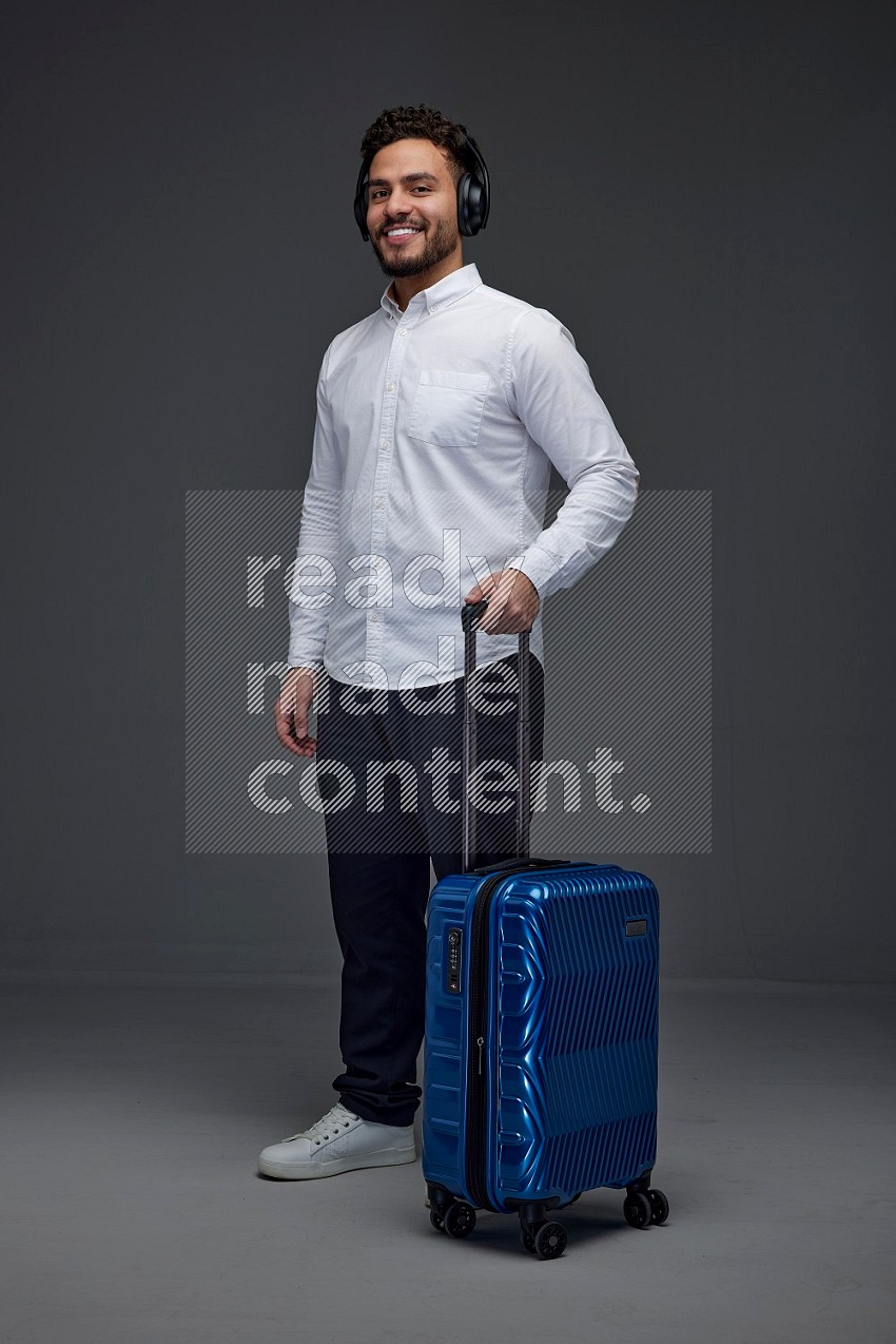 A man Posing with a carry-on with headsets  Wearing a White shirt on a grey background