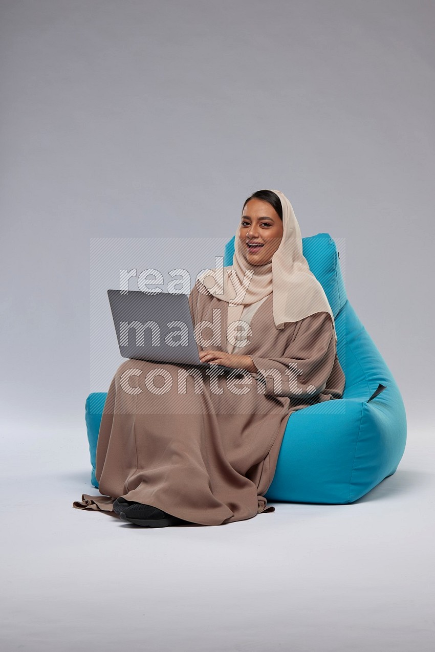 A Saudi woman sitting on a blue beanbag and working on laptop