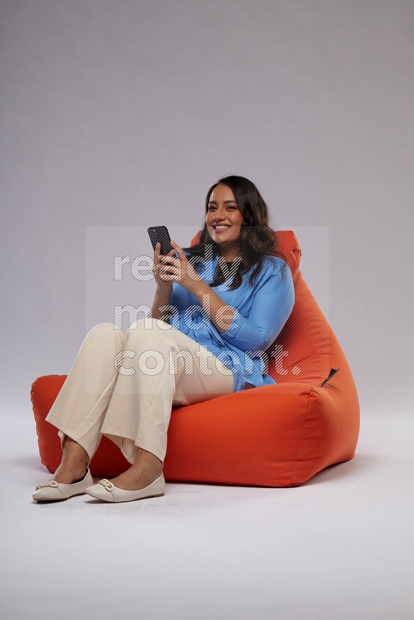 A woman sitting on an orange beanbag and texting on phone