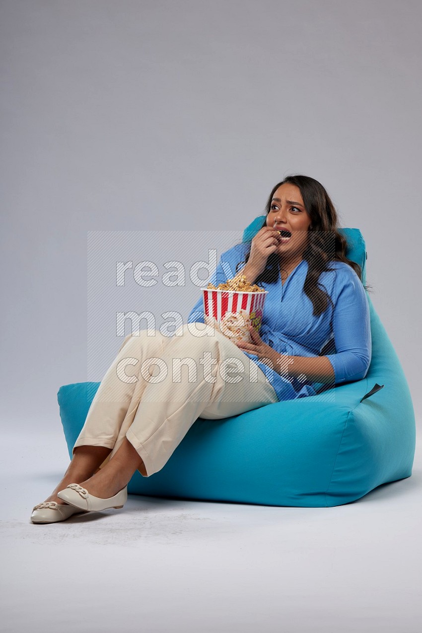 A woman sitting on a blue beanbag and eating popcorn