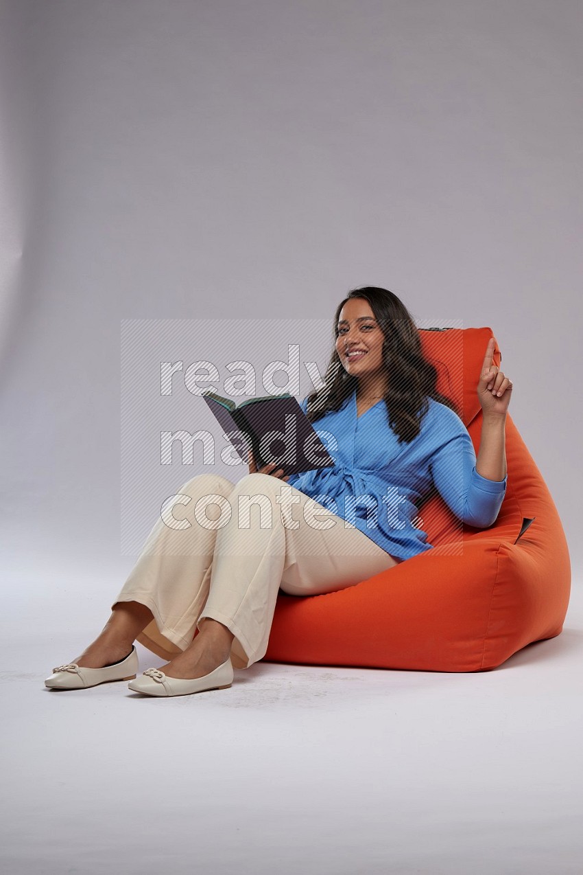 A woman sitting on an orange beanbag and reading a book