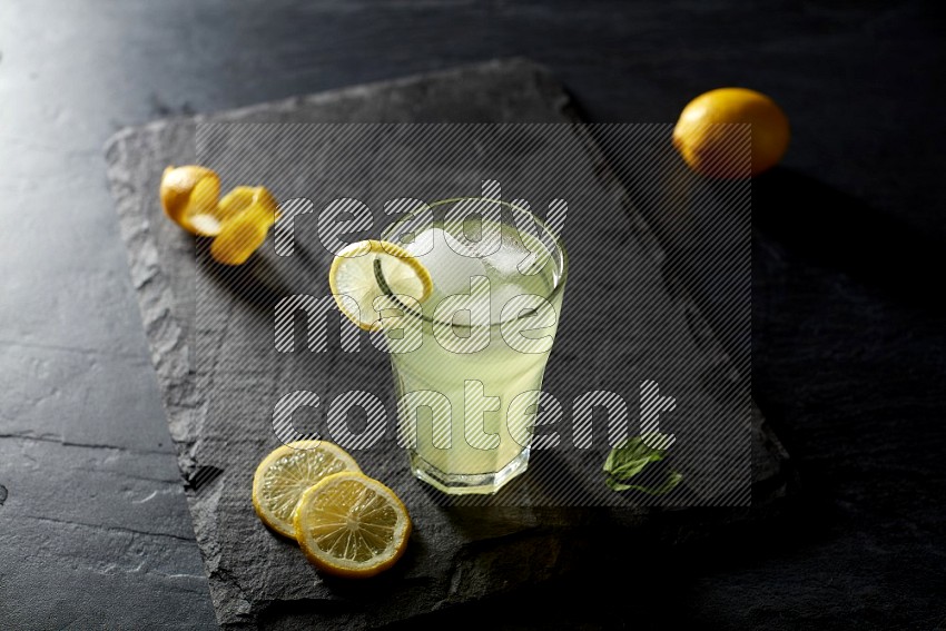 A glass of lemon juice with a lemon slice on black background