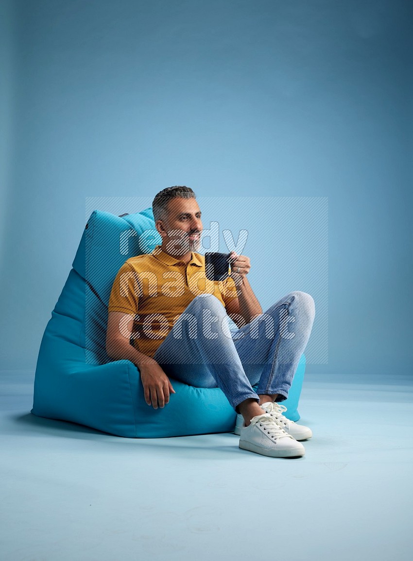 A man sitting on a blue beanbag and drinking coffee