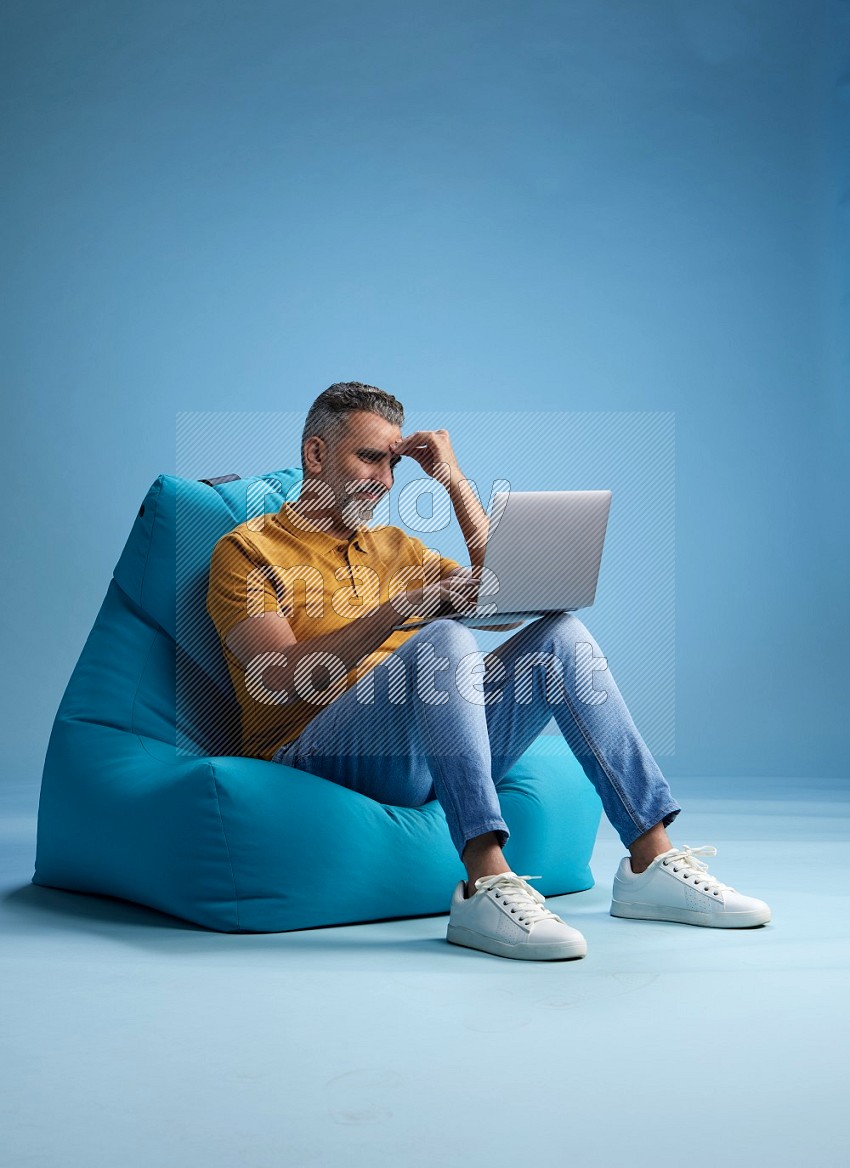 A man sitting on a blue beanbag and working on laptop