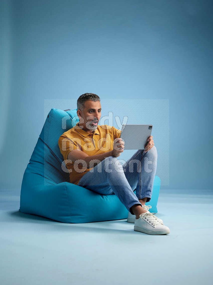 A man sitting on a blue beanbag and working on tablet